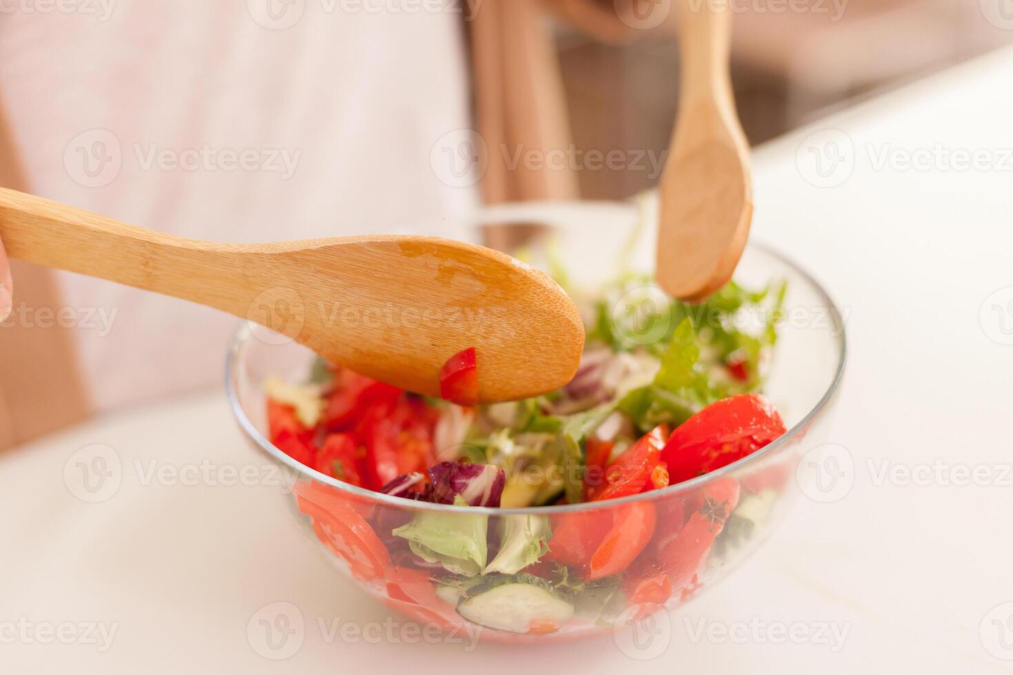 Hand mixing fresh salad in kitchen on wooden table. photo