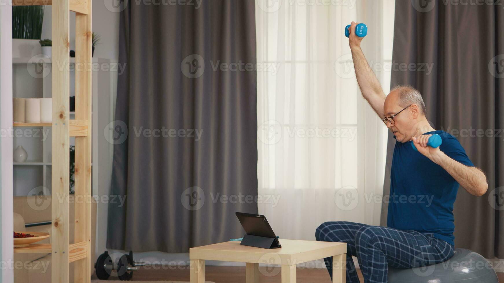 Grandfather training in living room with dumbbells watching online fitness program. Old person pensioner healthy training healthcare sport at home, exercising fitness activity at elderly age photo