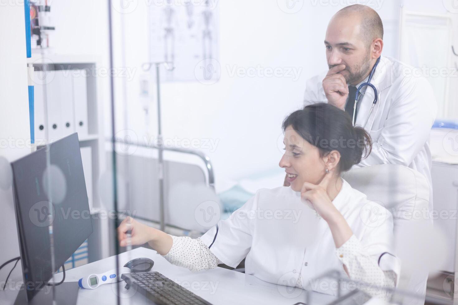 Young couple of doctors analysing medical scan on computer discovering the right treatment. Cardiologist showing and explaining results to his colleague using personal computer photo