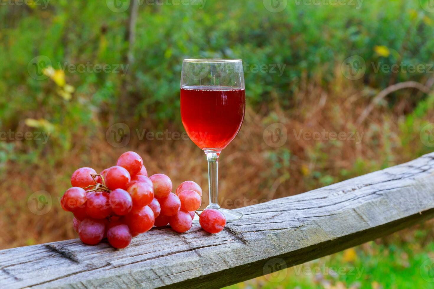 Red wine glass and bunch of grapes on wooden table photo