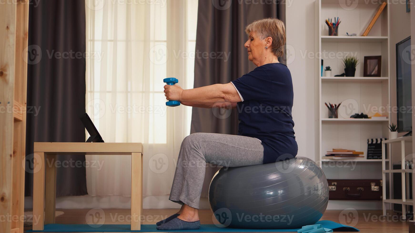 Senior woman exercising with dumbbells watching online lesson on tablet computer. Online training learning technology old woman lifting training healthy lifestyle sport fitness workout at home with weights dumbbell activity photo