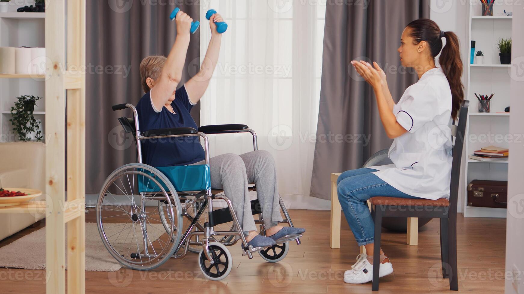 Old lady in wheelchair exercising with dumbbelss. Nurse helping with rehabilitation. Training, sport, recovery and lifting, old person retirement home, healthcare nursing, health support, social assistance, doctor and home service photo