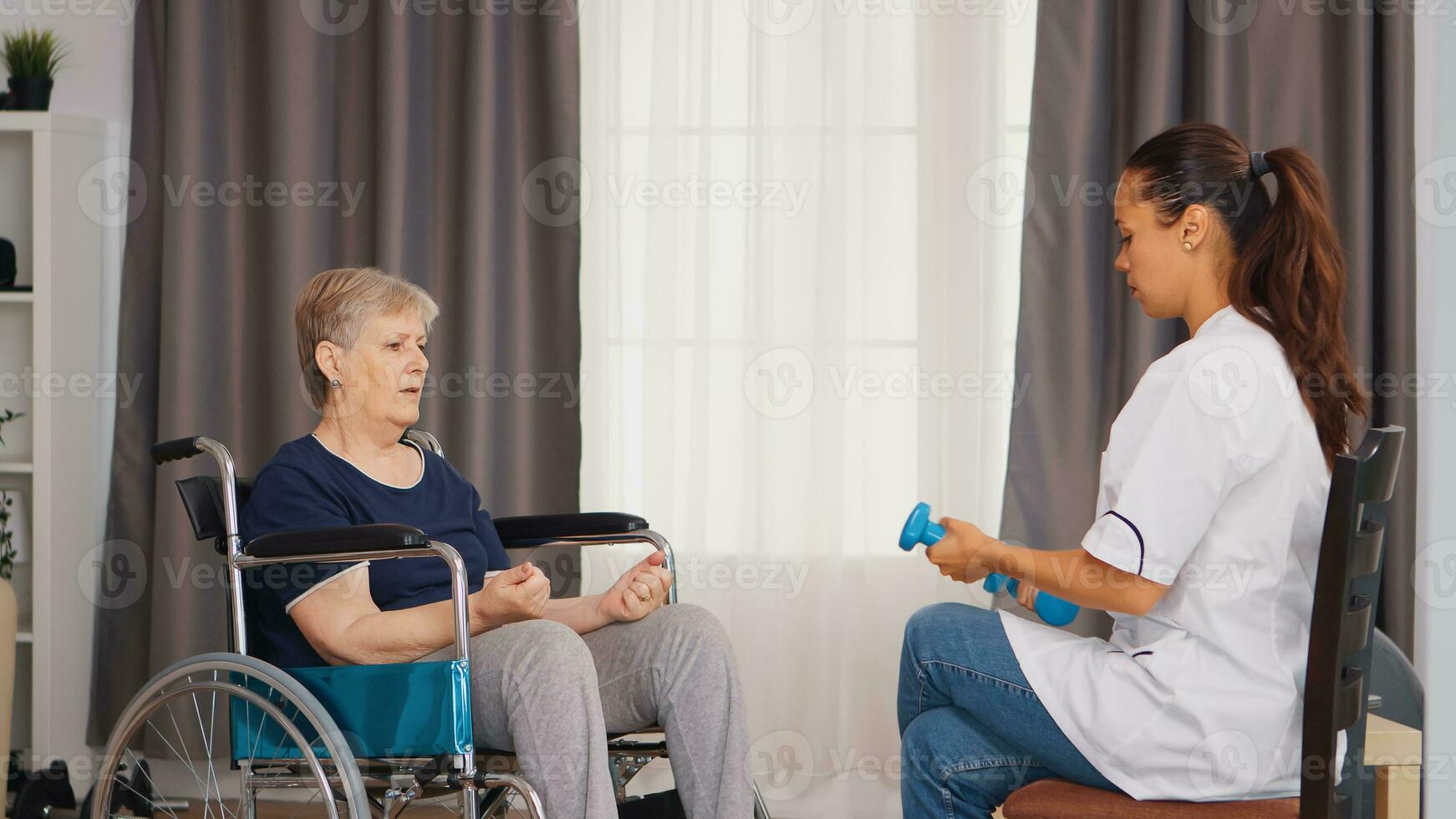 Senior woman in wheelchair doing rehabilitation with dumbbells with help from doctor. Training, sport, recovery and lifting, old person retirement home, healthcare nursing, health support, social assistance, doctor and home service photo