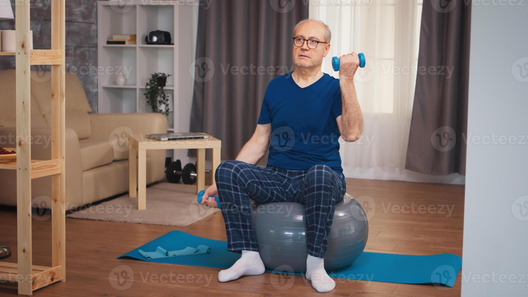 Old man doing biceps training with dumbbells on stability ball. Old person pensioner healthy training healthcare sport at home, exercising fitness activity at elderly age photo