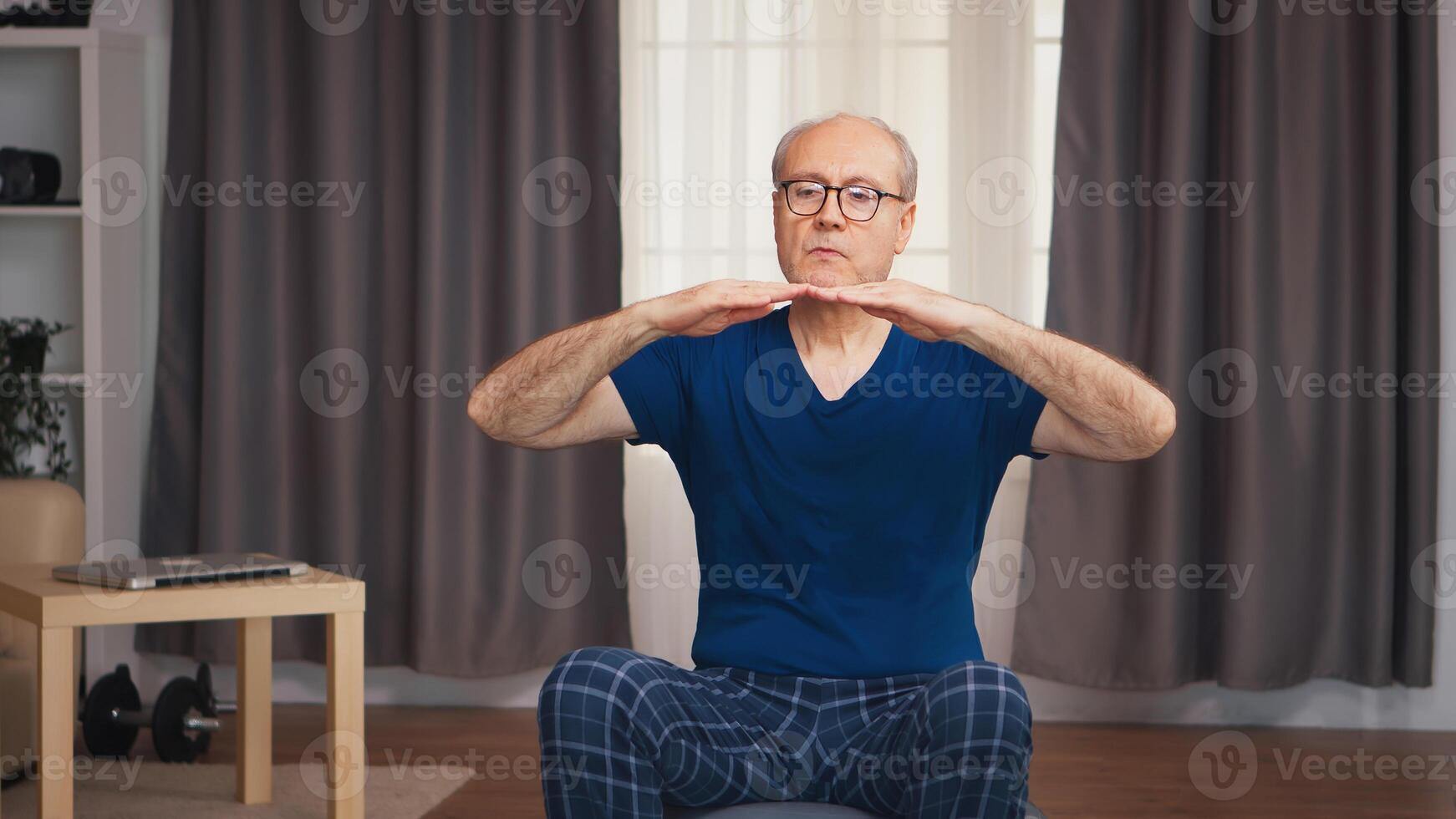 Elderly man exercising in living room sitting on stability ball. Old person pensioner healthy training healthcare sport at home, exercising fitness activity at elderly age photo