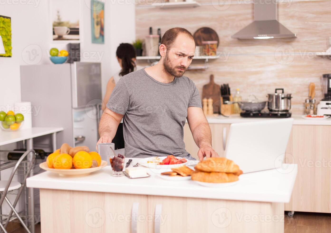 Frustrated self employed checking his mail in the morning sitting in the kitchen. Unhappy, stressed, frustrated furious negative and upset freelancer in pajamas yelling during morning meal at home photo