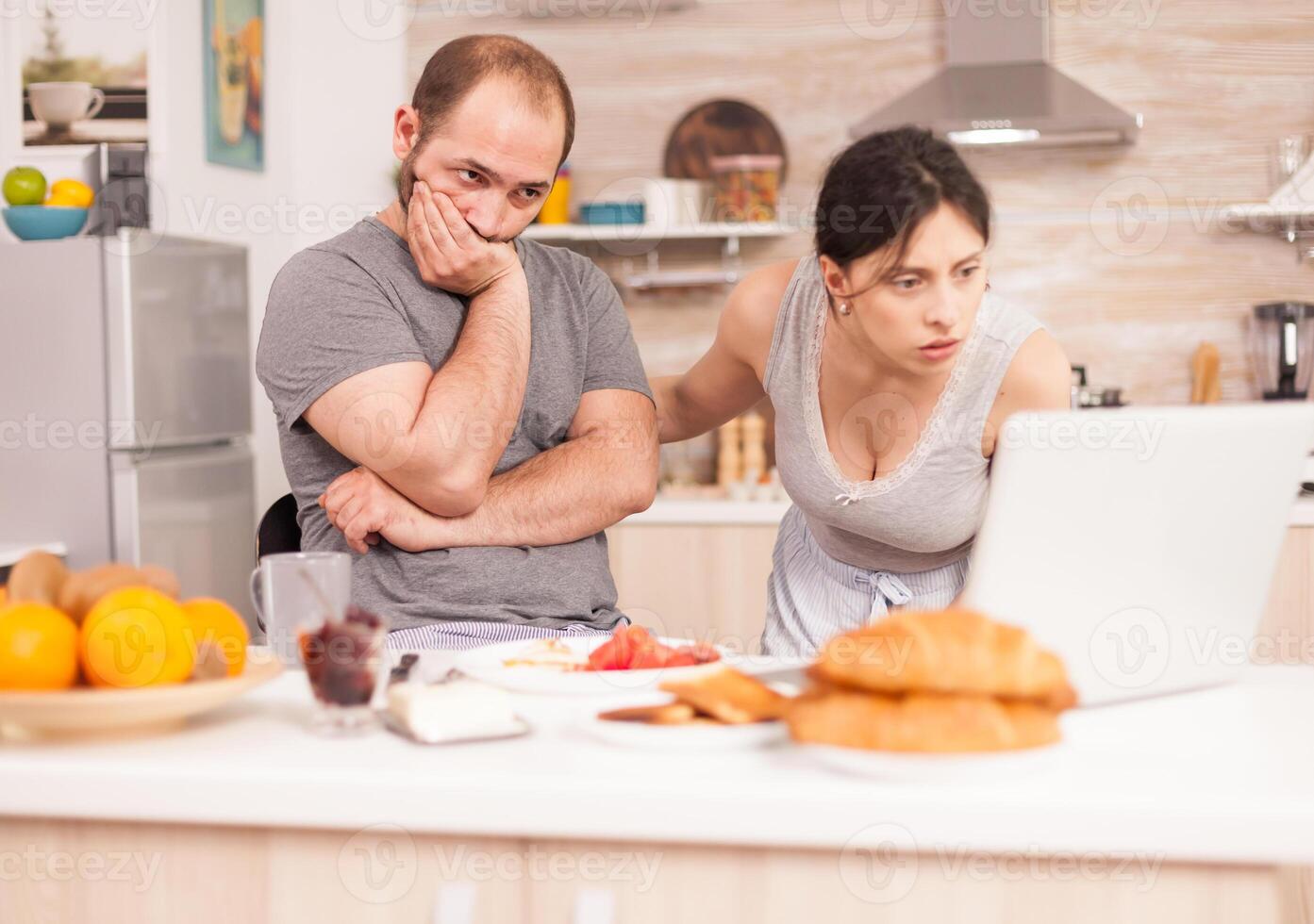 Couple worried about the bad news husband received in the morning during breakfast. Unhappy, stressed, frustrated furious negative and upset freelancer in pajamas yelling during morning meal at home photo