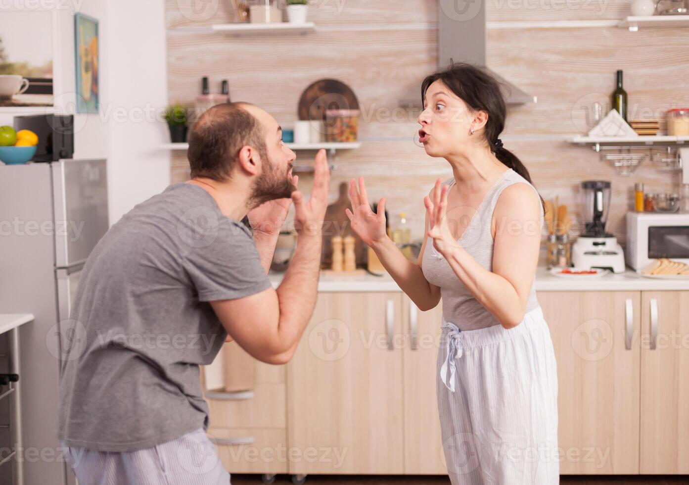 Couple screaming at each other in the kitchen in the morning. Young couple quarrels in the kitchen. Man and woman screams in frustration during home conversation. photo
