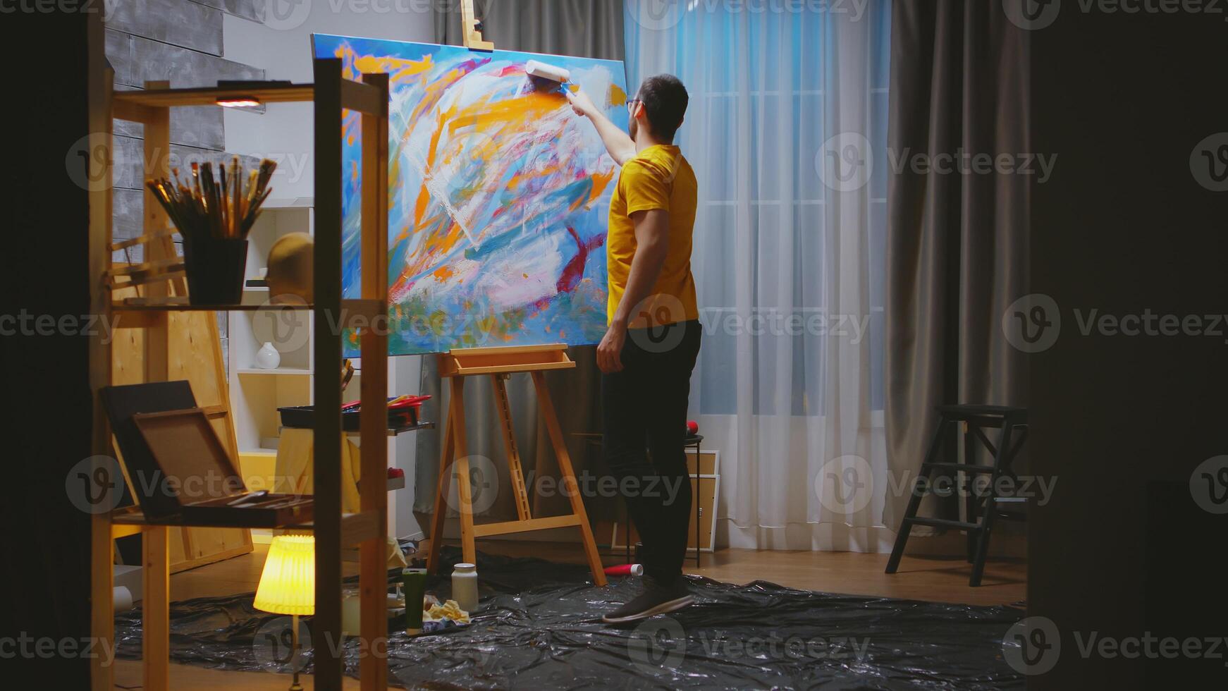 Successful artist painting with roller on large canvas in art workshop. photo