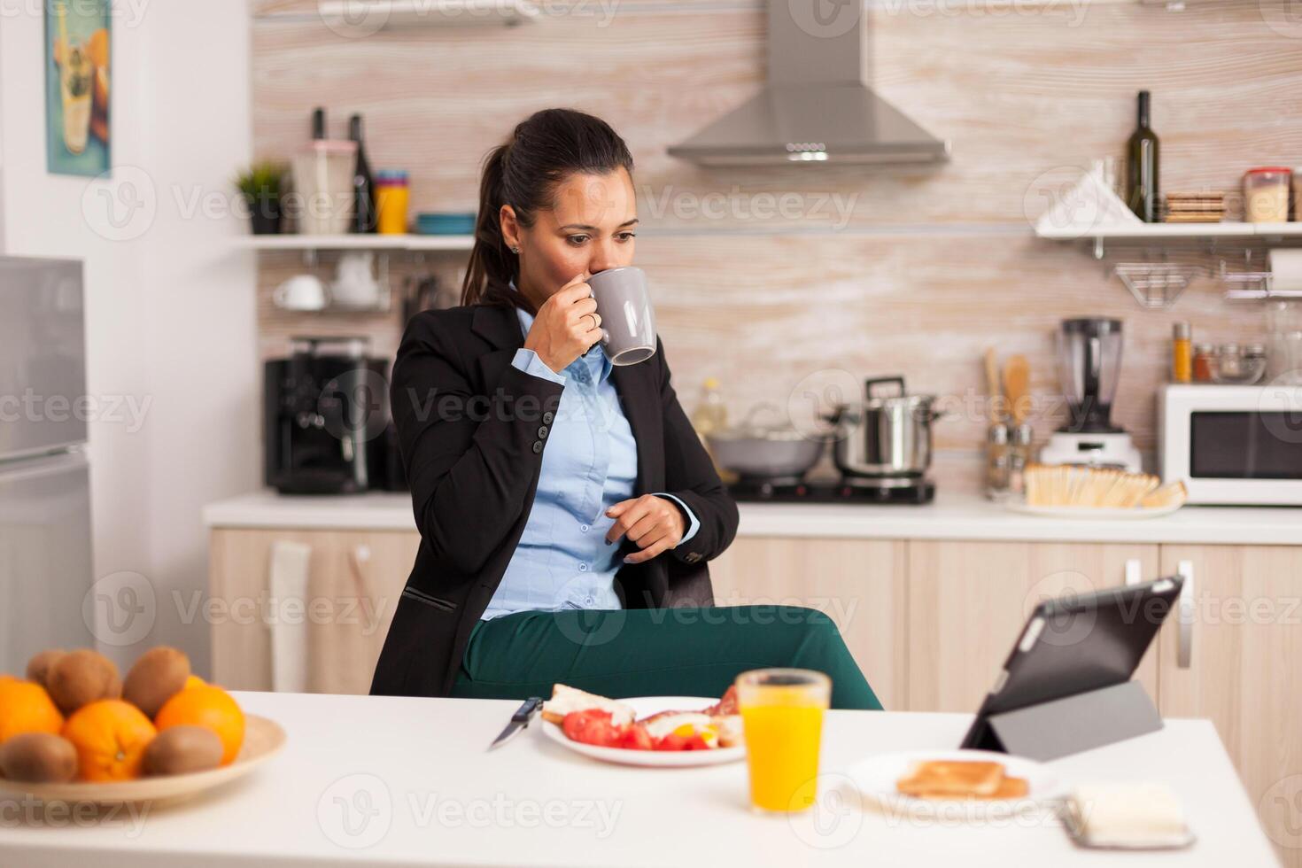Businesswoman enjoying her free time drinking a cup of coffee and using the tablet. Business woman reading the last news online before going to work, using modern technology in the kitchen while eating a healthy meal. photo