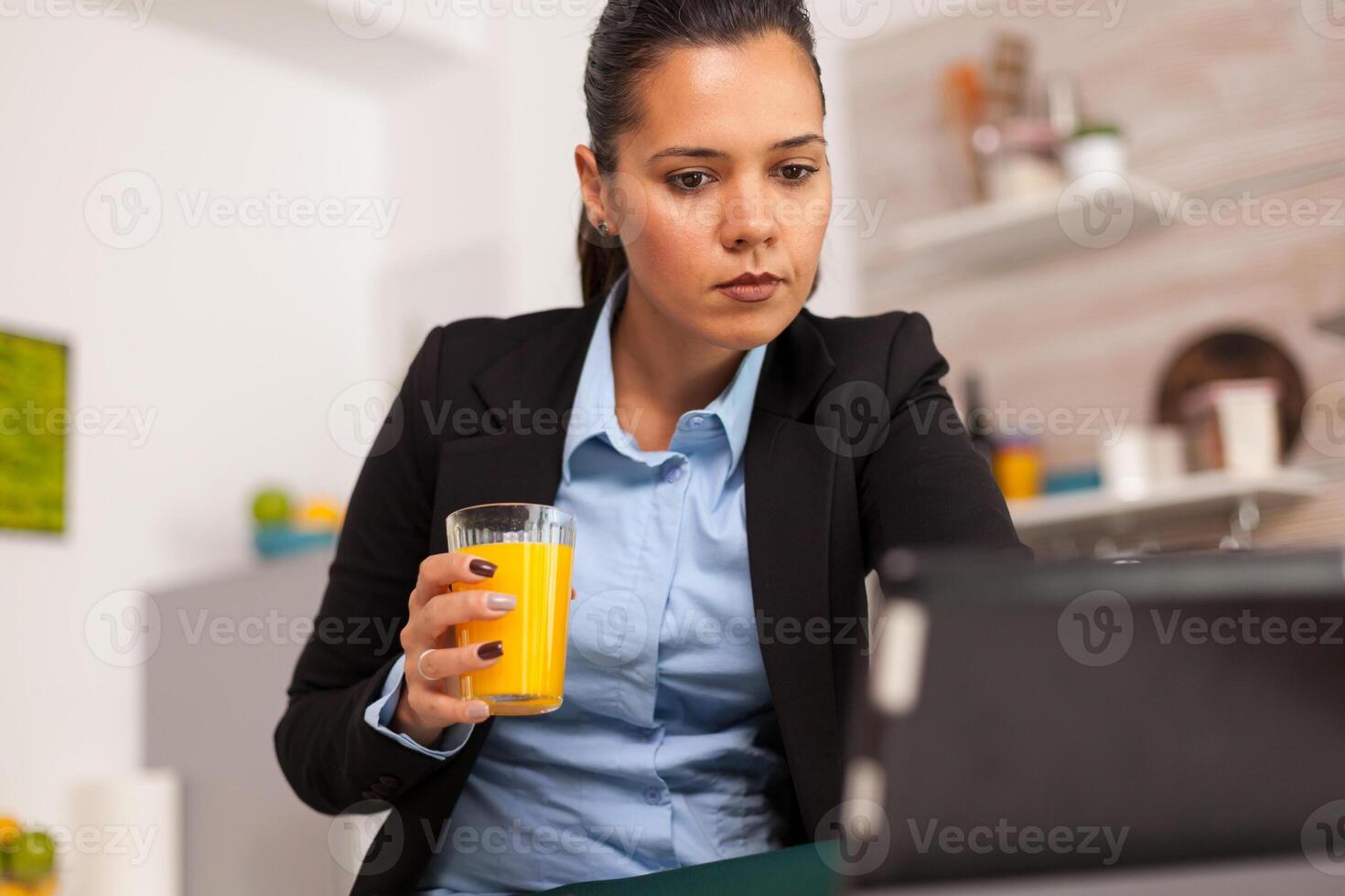 Businesswoman checking email at home in the kitchen drinking an orange juice. Business woman reading the last news online before going to work, using modern technology in the kitchen while eating a healthy meal photo