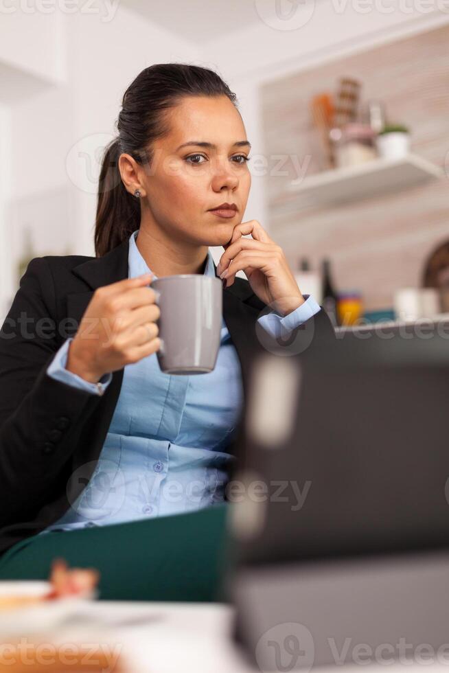 Freelancer drinking coffee in the morning on table top during breakfast using tablet computer. Business woman reading the last news online before going to work, using modern technology in the kitchen while eating a healthy meal photo