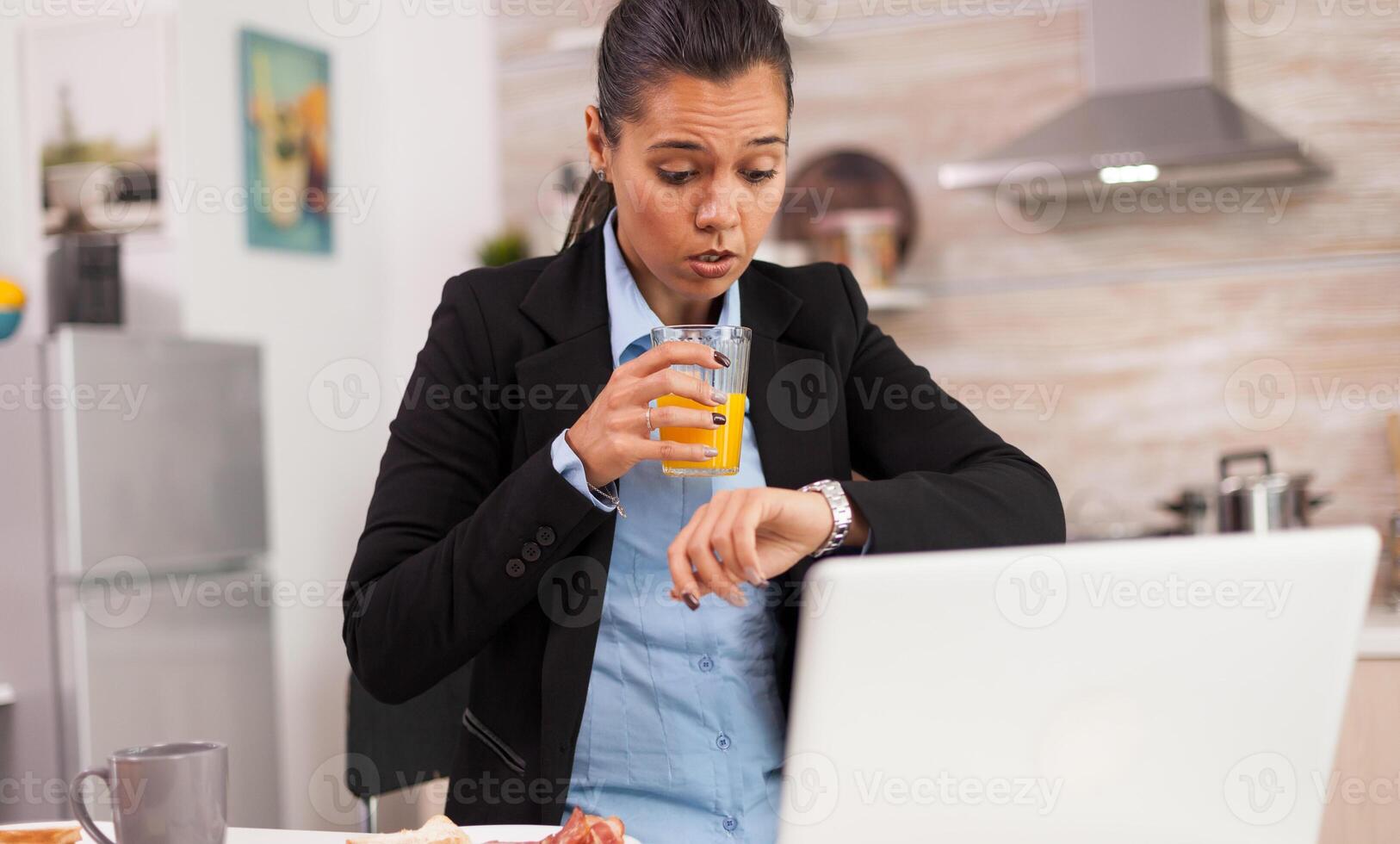 Freelancer late at work while eating breakfast in a hurry. Concentrated business woman in the morning multitasking in the kitchen before going to the office, stressful way of life, career and goals to meet photo
