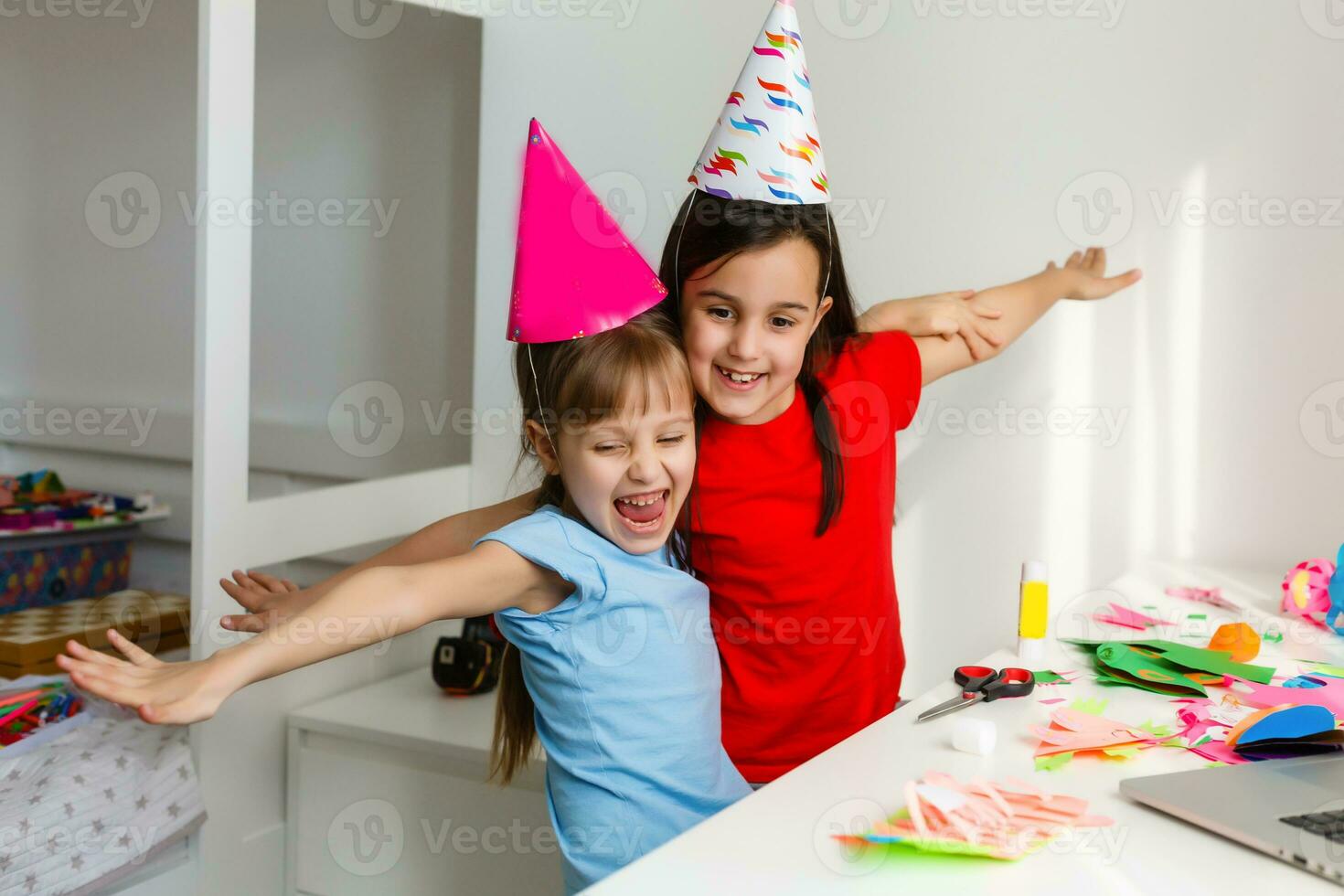 niños en línea cumpleaños fiesta. pequeño muchachas en vestidos, sombrero celebrar fiesta con amigos. conferencia, vídeo llamada en computadora portátil, computadora. cuarentena, coronavirus pandemia COVID-19. foto