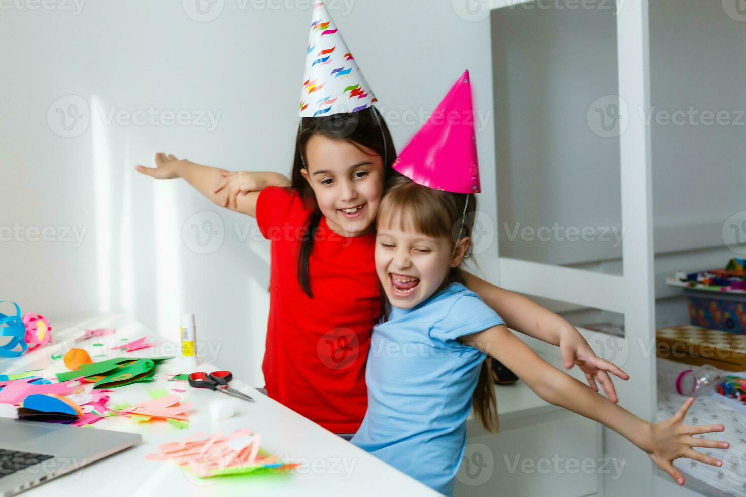 niños en línea cumpleaños fiesta. pequeño muchachas en vestidos, sombrero celebrar fiesta con amigos. conferencia, vídeo llamada en computadora portátil, computadora. cuarentena, coronavirus pandemia COVID-19. foto