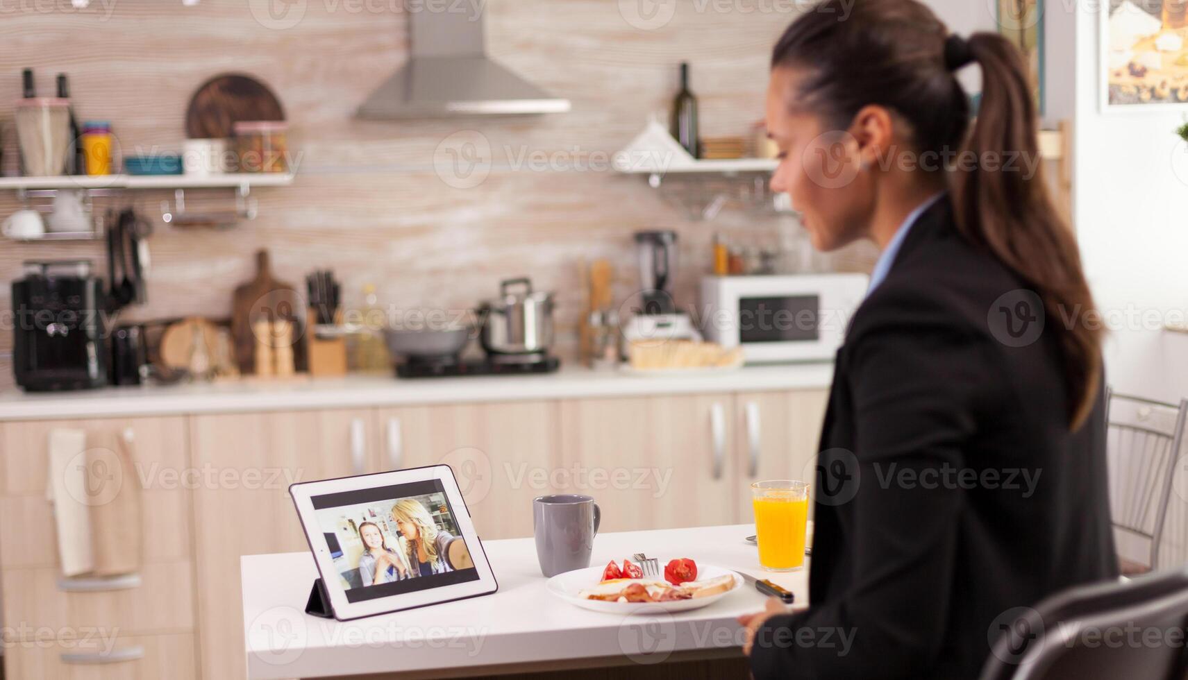 negocio mujer durante un vídeo llamada con amigos mientras comiendo desayuno antes de dejando a el oficina. utilizando moderno en línea Internet web tecnología a charla vía cámara web video conferencia aplicación con parientes, familia, amigos y compañeros de trabajo foto