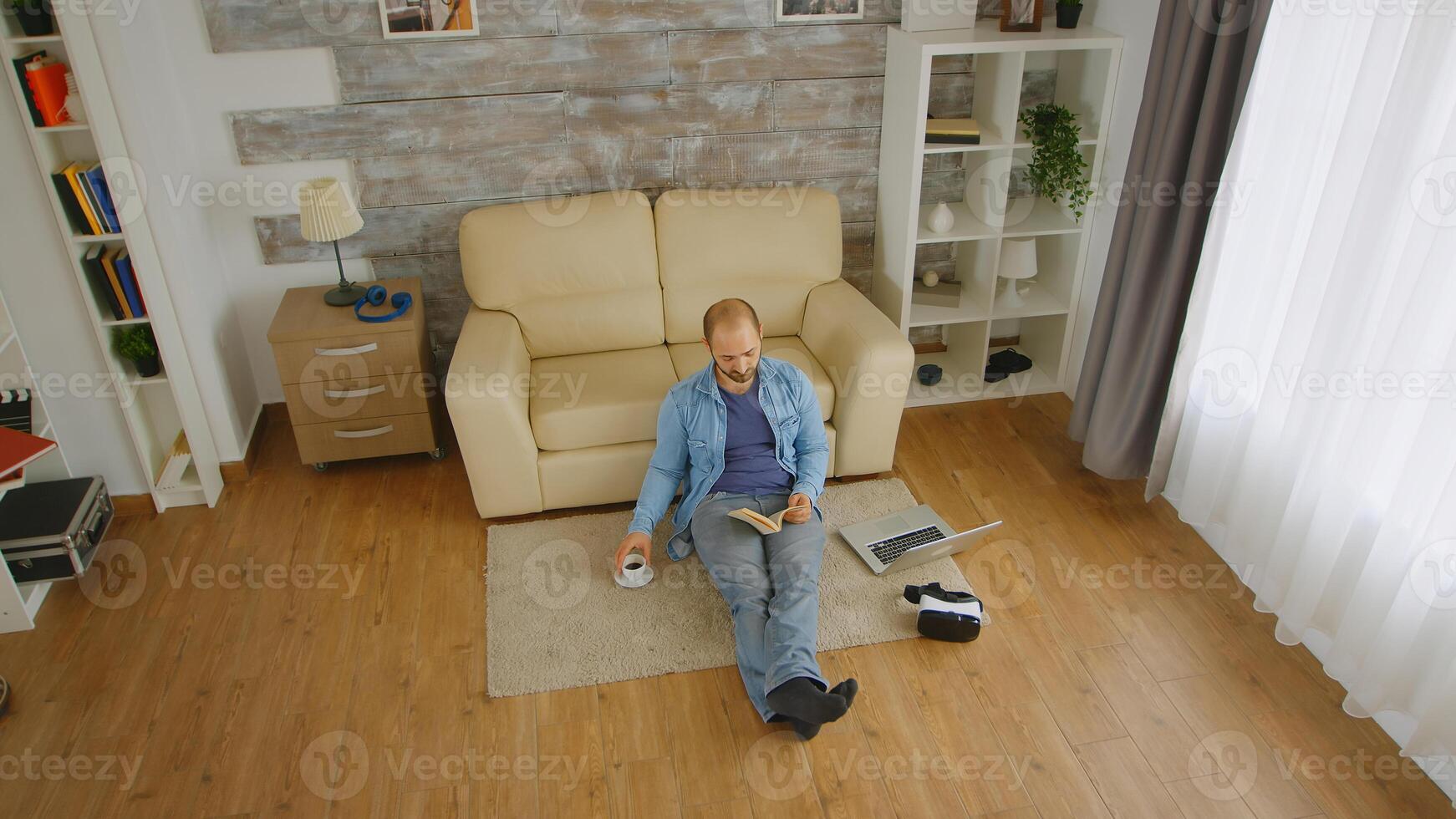 Bold young adult on the floor of his apartment reading a novel and drinking coffee on a lazy sunday photo