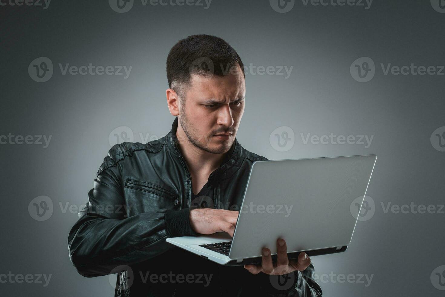 Man in black jacket looking at laptop, half turn. Holding opened laptop and working. Emotion. photo