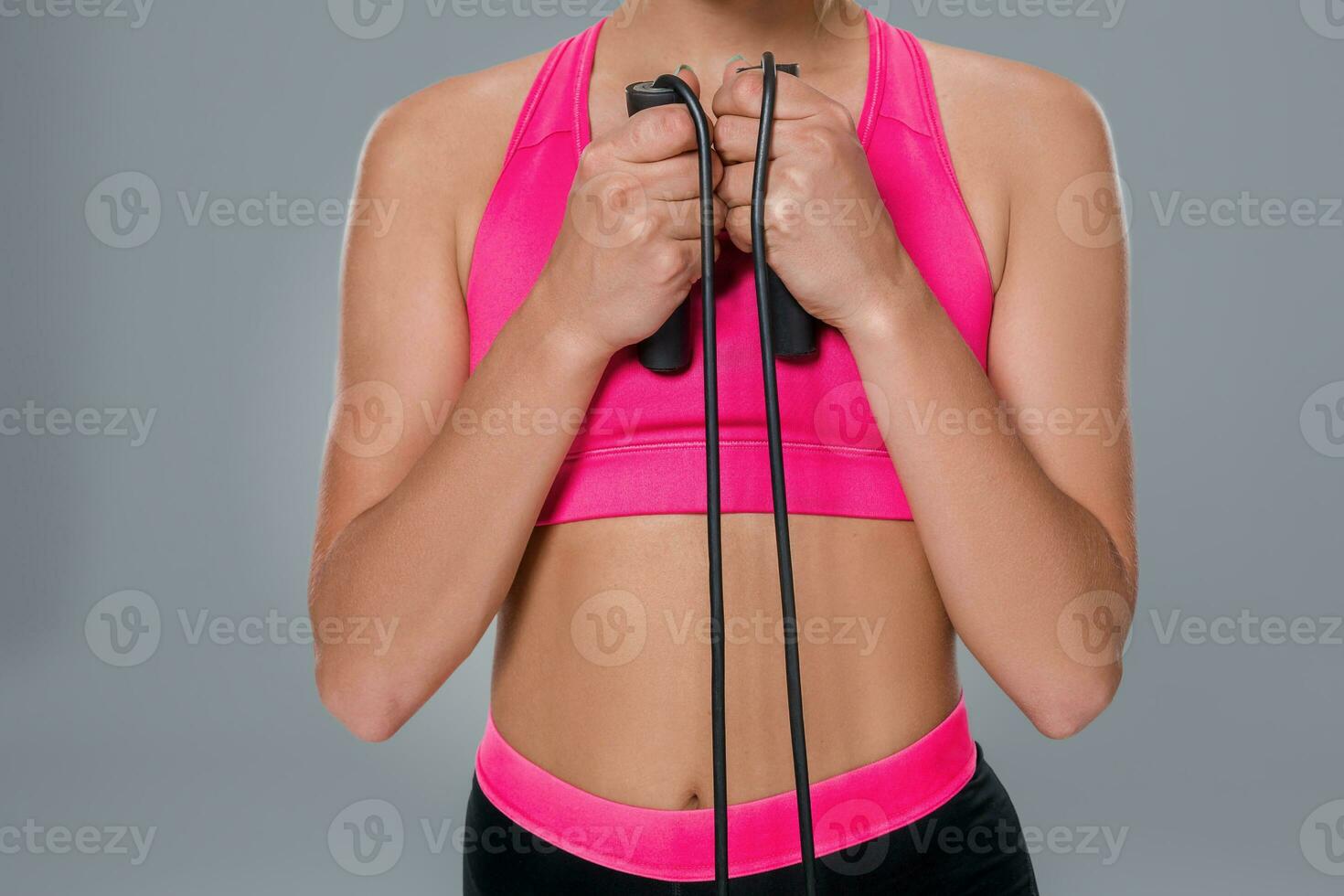 Full length image of a pretty fitness woman doing exercise with skipping rope over gray background. Close-up photo