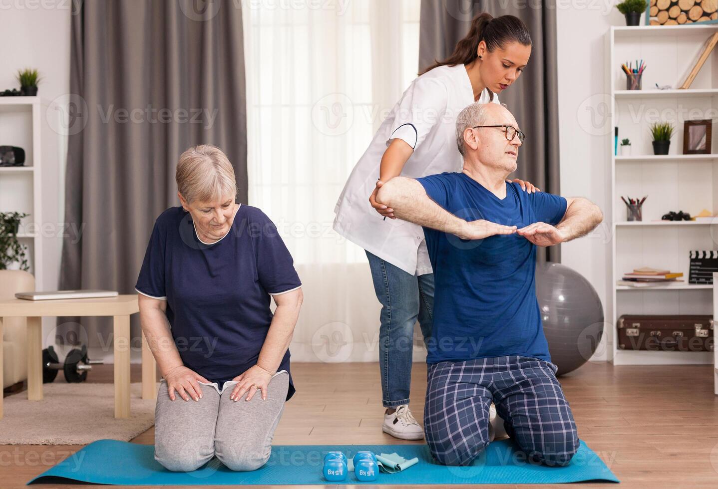The therapist helping the old man while his wife relaxes. Home assistance, physiotherapy, healthy lifestyle for senior old person, training and recovery with professional physiotherapist photo