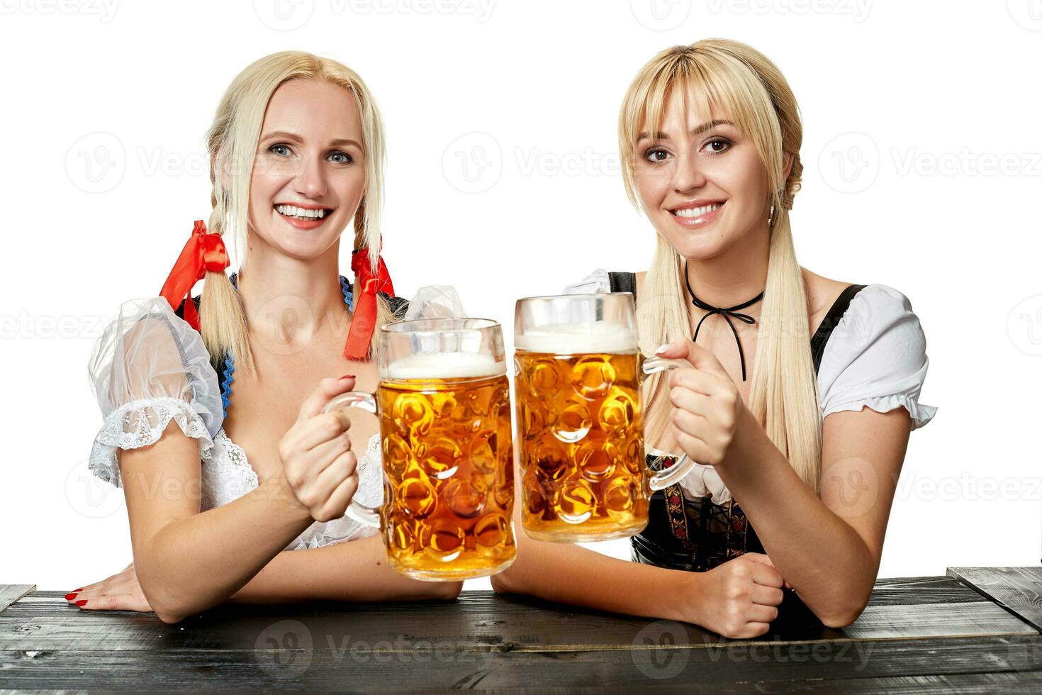 Two beautiful women holding a glass of beer while sitting at a wooden table on a white background in the studio photo