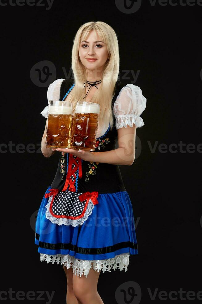 Young sexy woman wearing a dirndl with two beer mugs on black background. photo