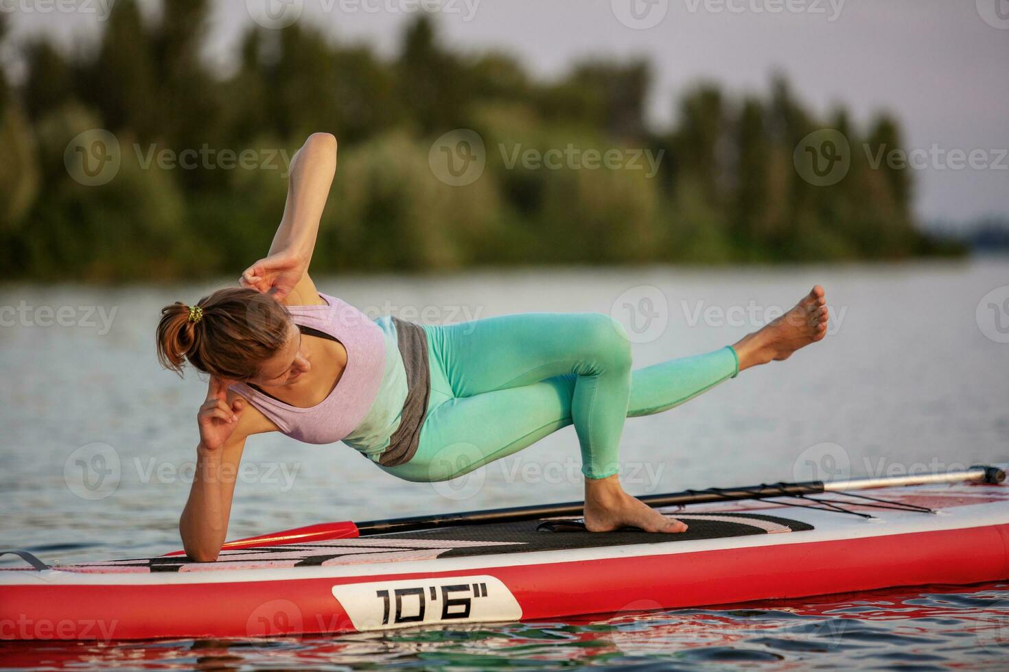 Sporty woman in yoga position on paddleboard, doing yoga on sup board, exercise for flexibility and stretching of muscles photo
