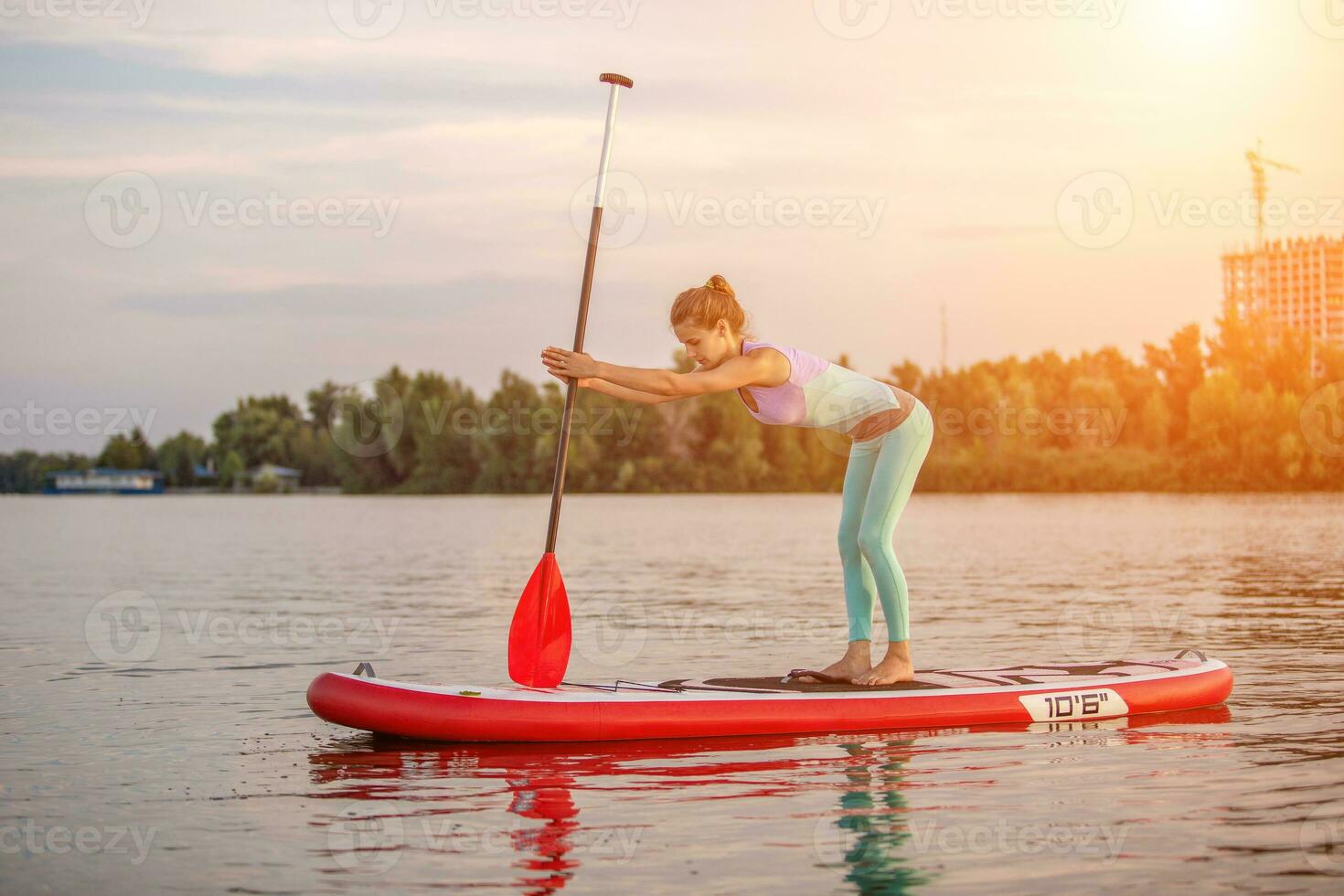 Sporty woman in yoga position on paddleboard, doing yoga on sup board, exercise for flexibility and stretching of muscles photo