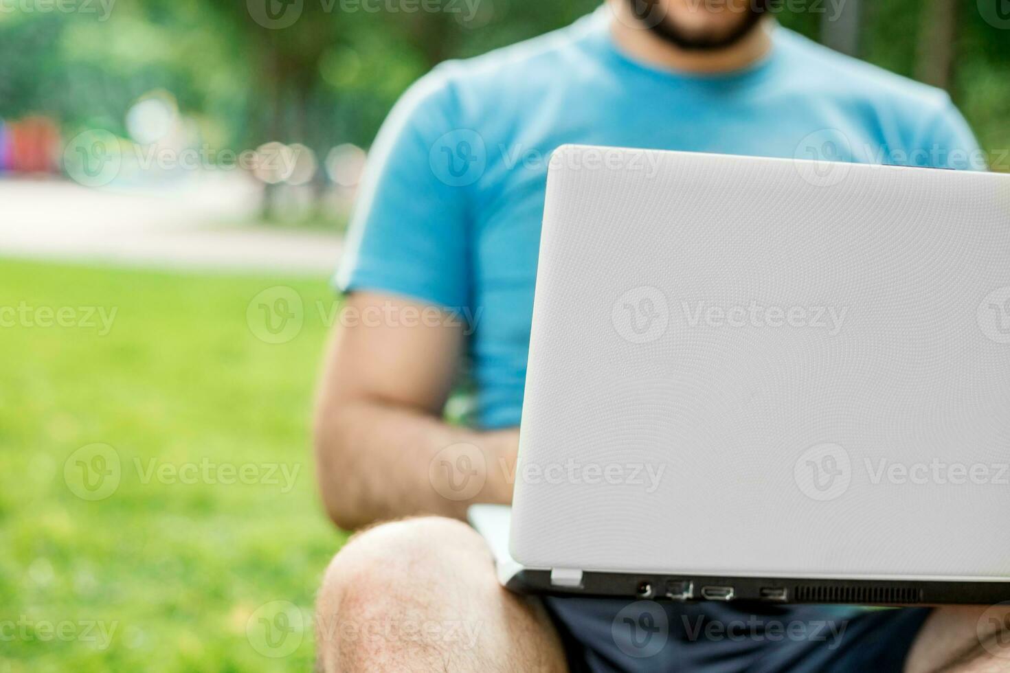 Young man using and typing laptop computer in summer grass. photo