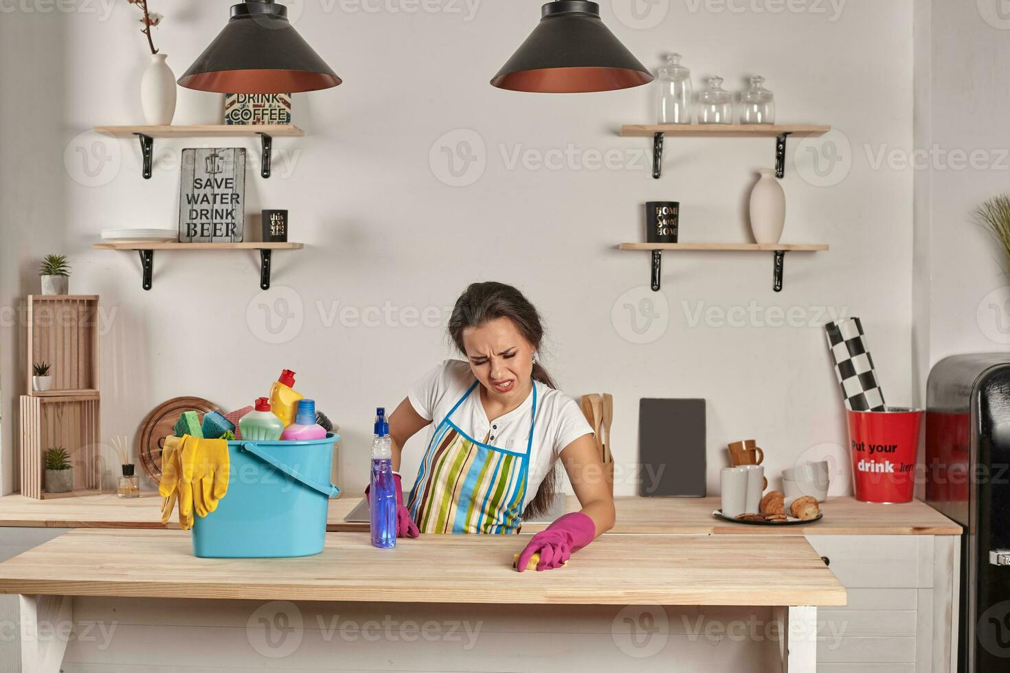 Beautiful cheerful brunette woman in gloves cleaning modern kitchen photo
