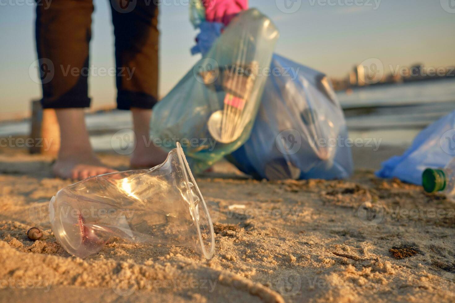 Young volunteer in purple gloves is walking with garbage bag along a dirty beach of the river and cleaning up trash. People and ecology. Close-up. photo