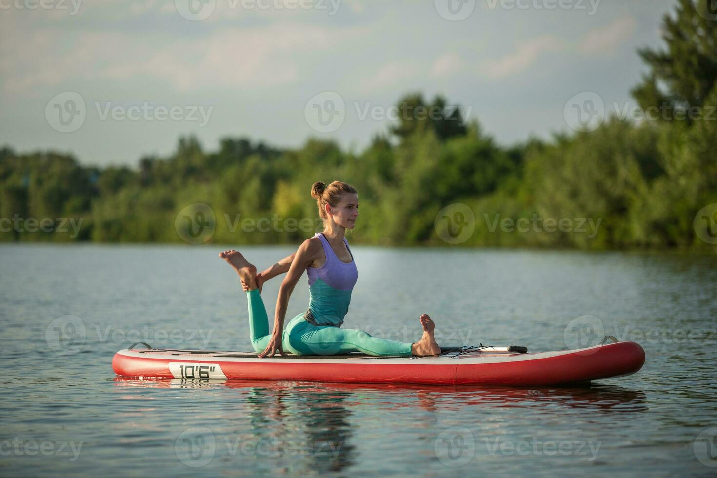 Young woman doing yoga on sup board with paddle. Meditative pose, side view - concept of harmony with the nature photo
