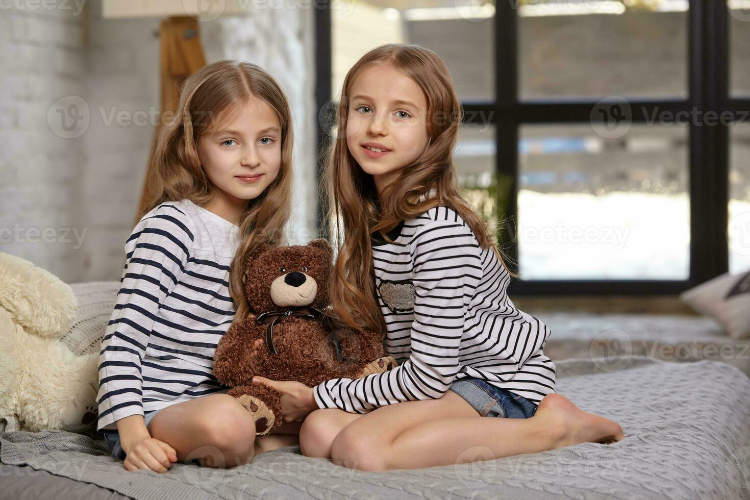 The image of two little sisters sitting on the bed in the room. photo