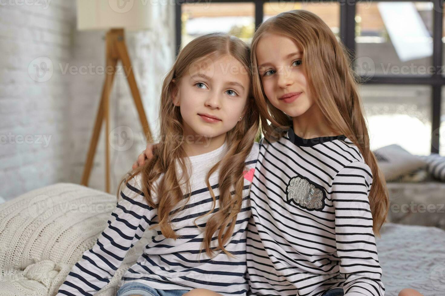 The image of two little sisters sitting on the bed in the room. photo