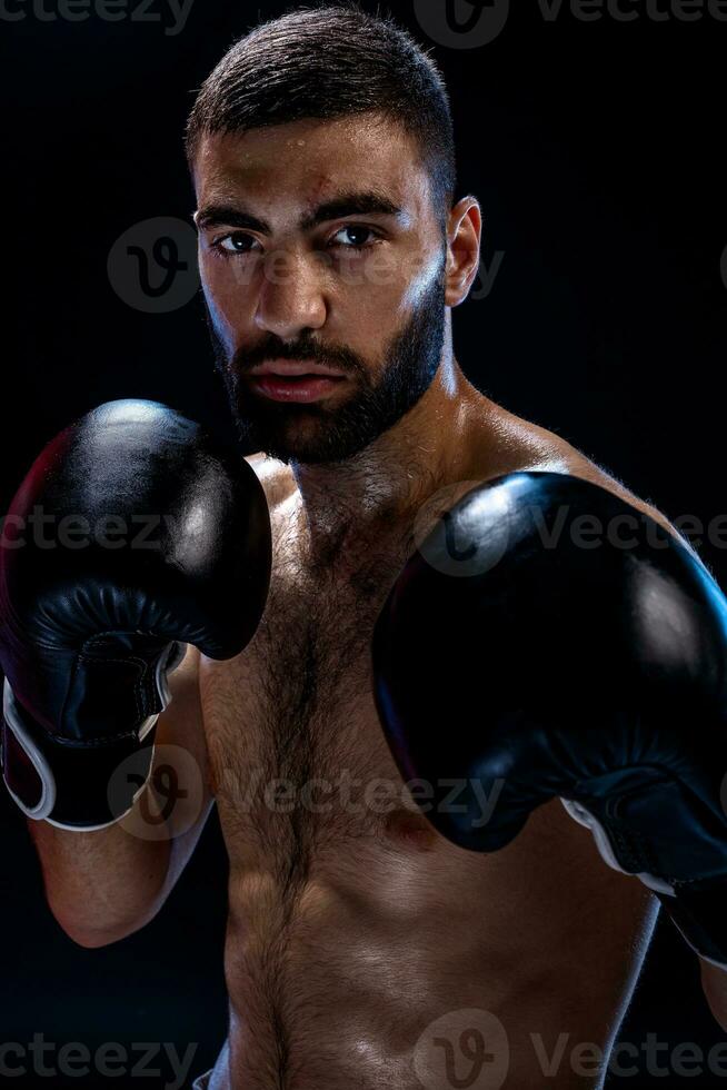 Strong muscular boxer in black boxing gloves. A man in a boxing stand on black background. photo