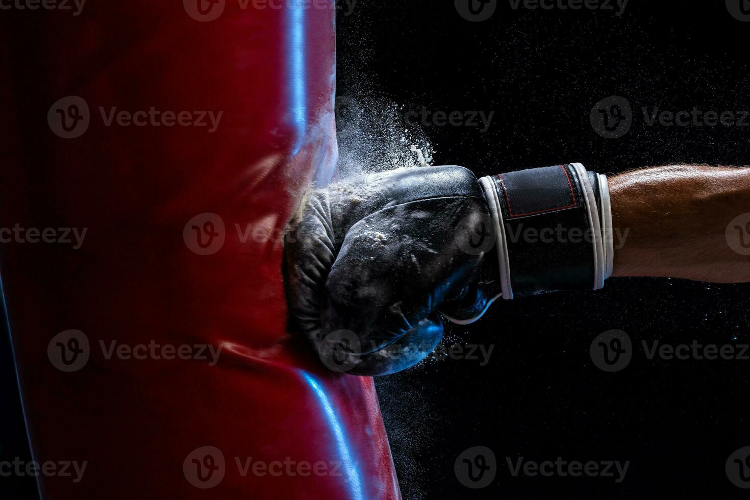 Close-up hand of boxer at the moment of impact on punching bag over black background photo