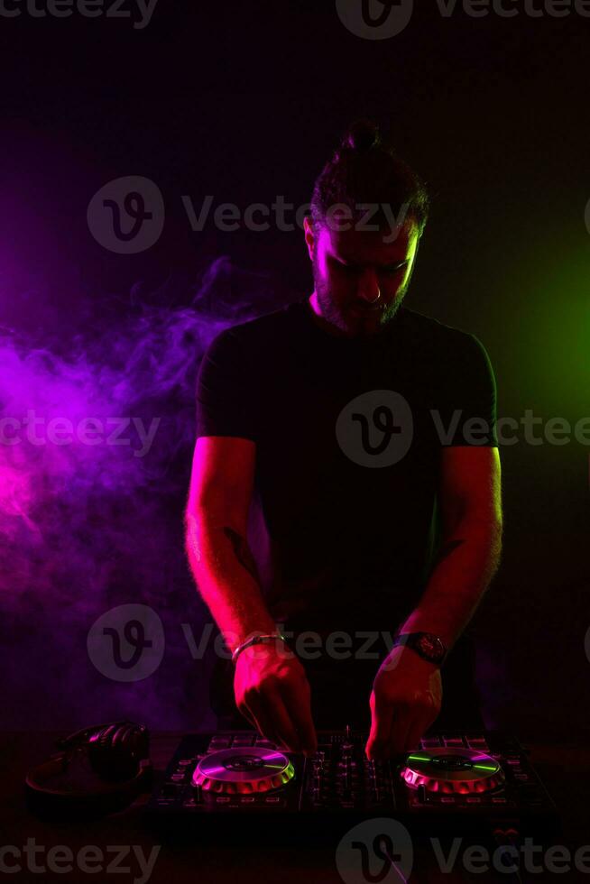 Attractive young DJ playing on turntables with color light effects photo