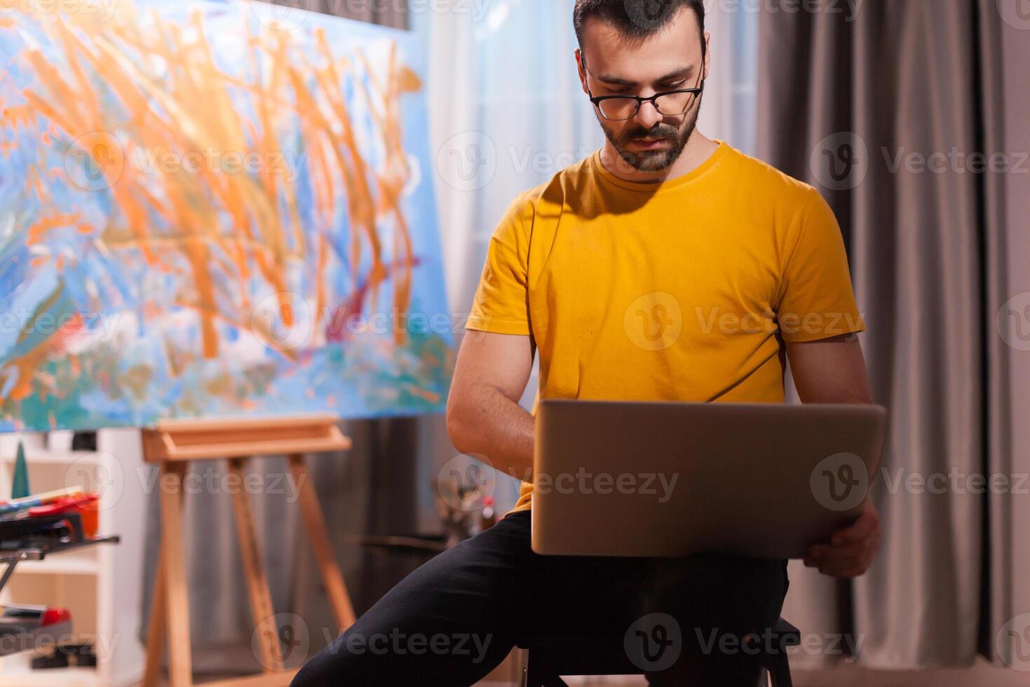 Painter using laptop on art workshop. Modern artwork paint on canvas, creative, contemporary and successful fine art artist drawing masterpiece photo