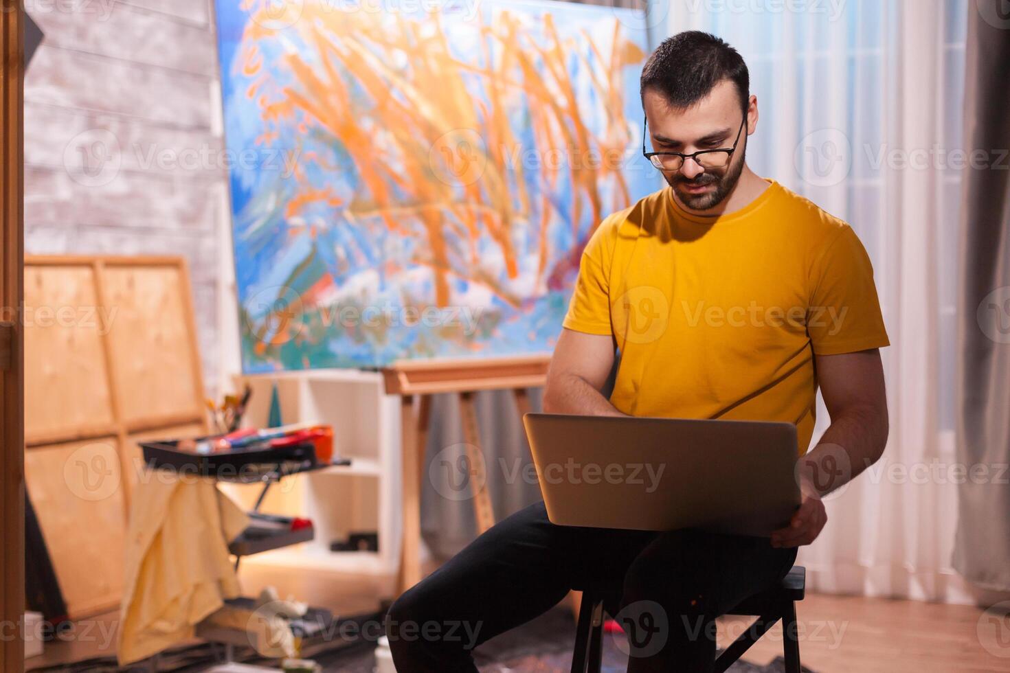 Man painter in studio searching for inspiration on laptop in art studio. Modern artwork paint on canvas, creative, contemporary and successful fine art artist drawing masterpiece photo
