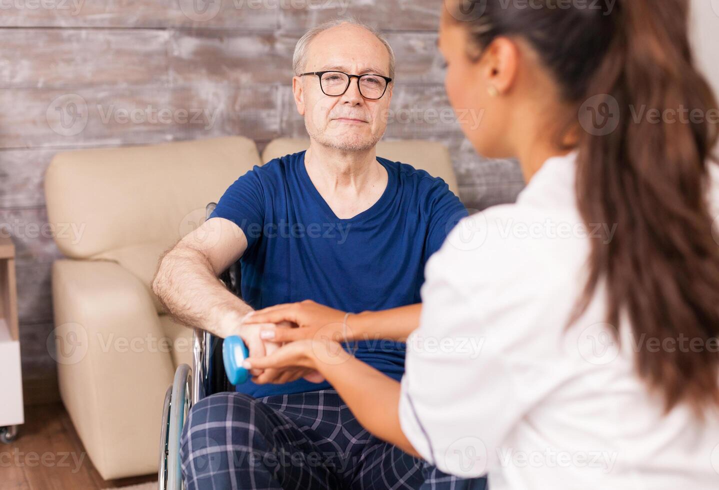 Caregiver helping paralyzed man to recover using dumbbells for the arms muscles. Disabled handicapped old person with social worker in recovery support therapy physiotherapy healthcare system nursing retirement home photo