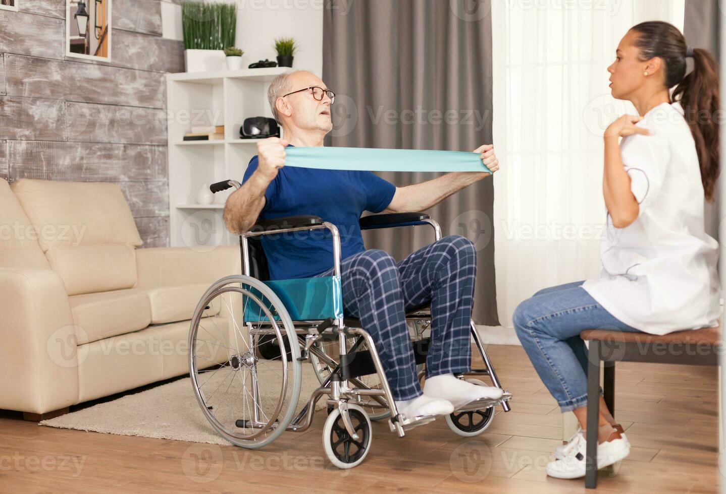 Disabled senior patient working out at home with resistance band under the guidance of a nurse. Disabled handicapped old person with social worker in recovery support therapy physiotherapy healthcare system nursing retirement home photo