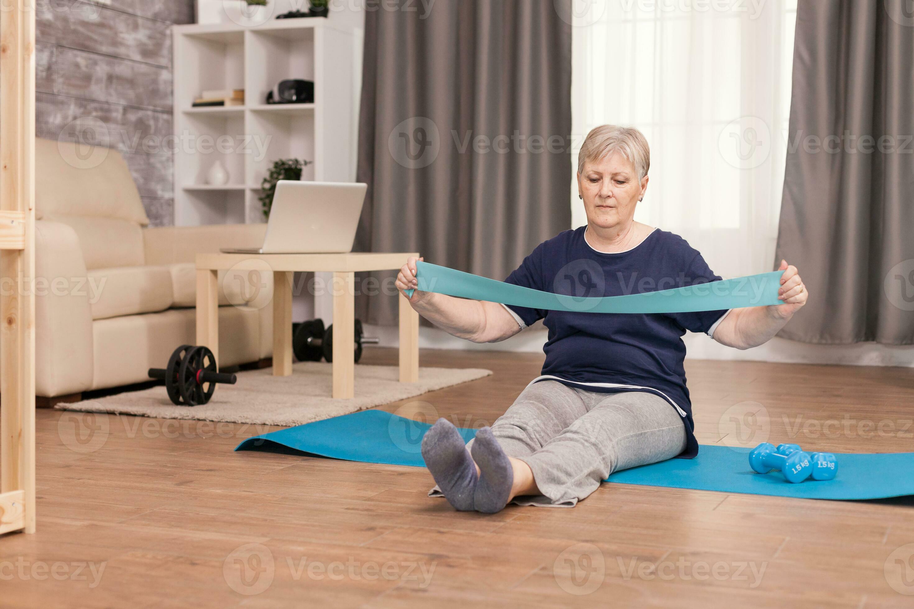 Active grandma using resistance band sitting on yoga mat at home