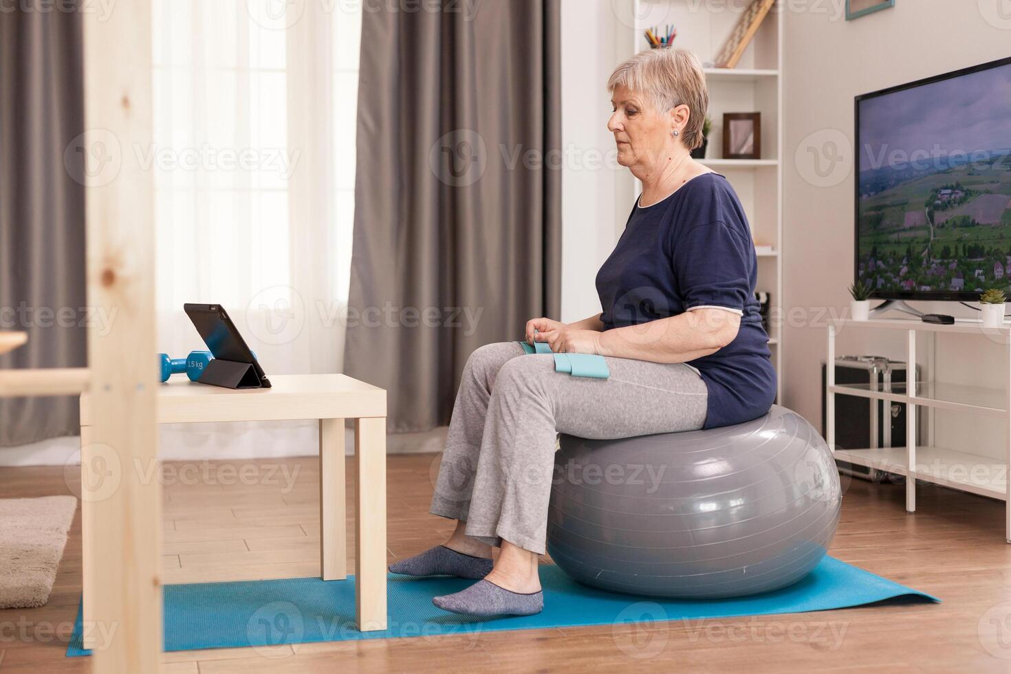 Elderly woman learning sport online sitting on balance ball in front of
