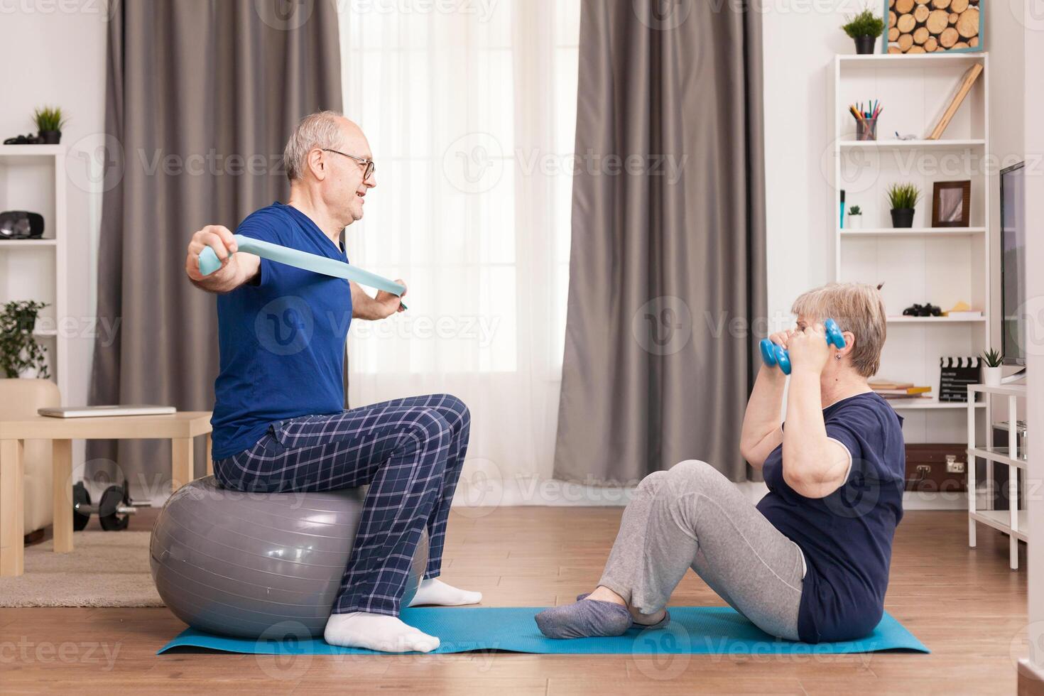 Senior couple exercising in living room using yoga mat and stability ball. Old person healthy lifestyle exercise at home, workout and training, sport activity at home on yoga mat. photo