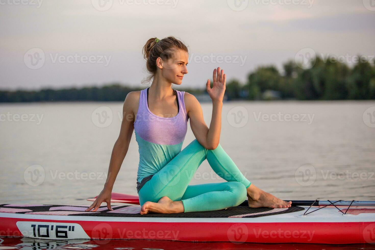 Young woman sitting on paddle board, practicing yoga pose. Doing yoga exercise on sup board, active summer rest photo