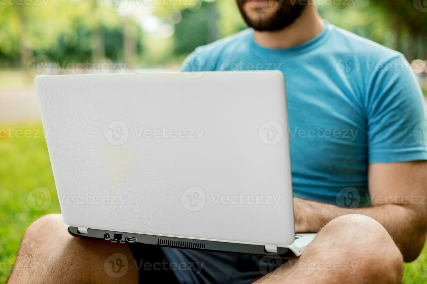 Young man using and typing laptop computer in summer grass. photo