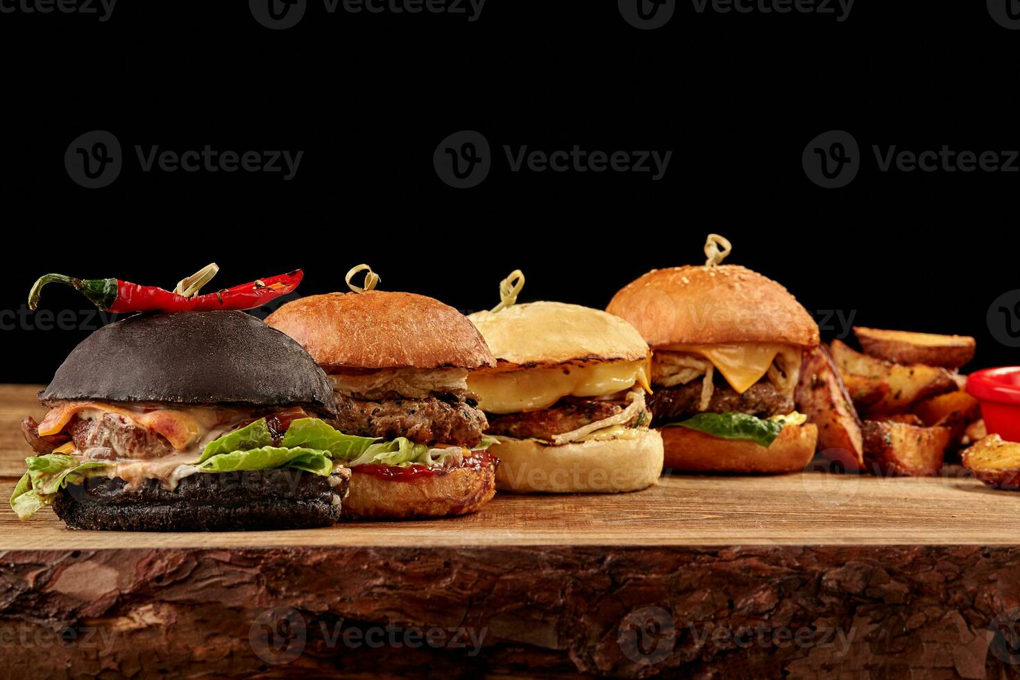 Set of burgers with meat, cheese, tomatoes, mayonnaise on wooden table, black background. Space for text. photo