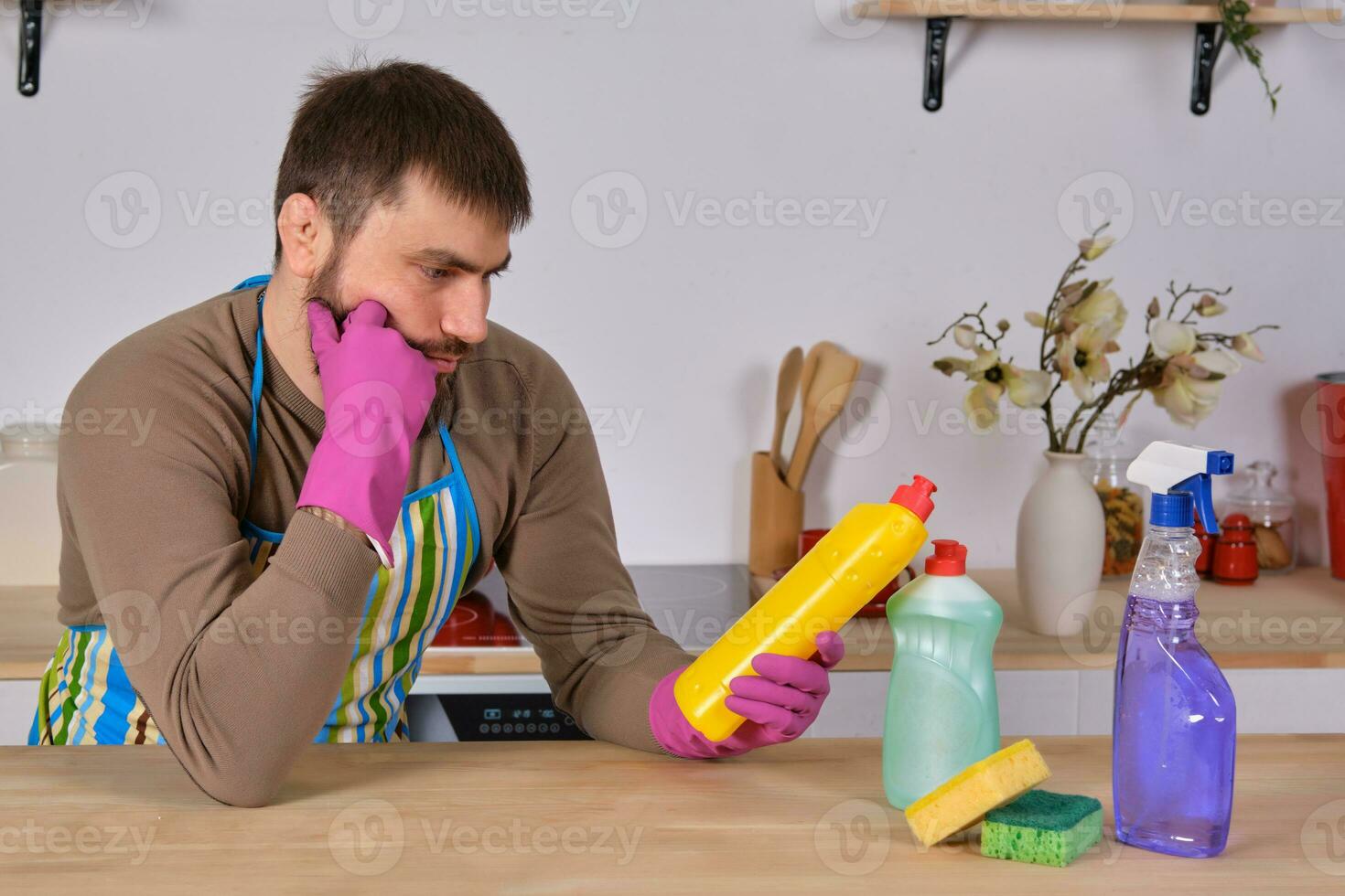 Young man wanted to help his wife in housecleaning, but he doesn't know what to do with all of detergents photo