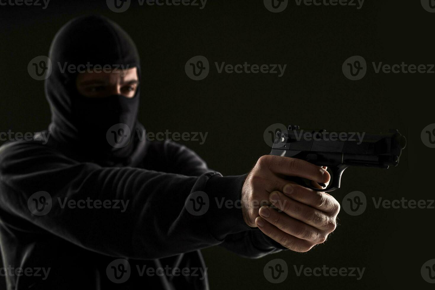 The robber in a mask with a gun pointed to the side on a black background photo