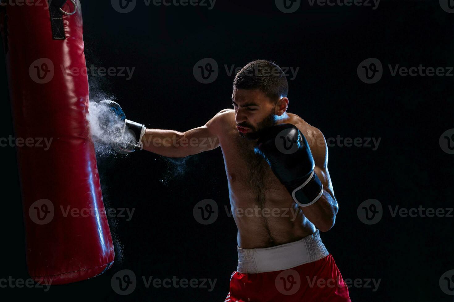 muscular hermoso Boxer dando un potente adelante patada durante un práctica redondo con un boxeo bolsa. foto